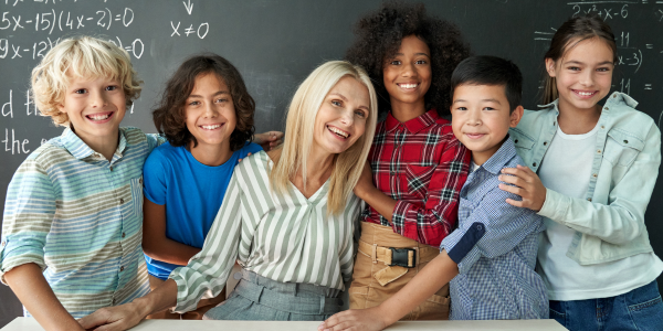 teacher sitting at her desk surrounded by happy students